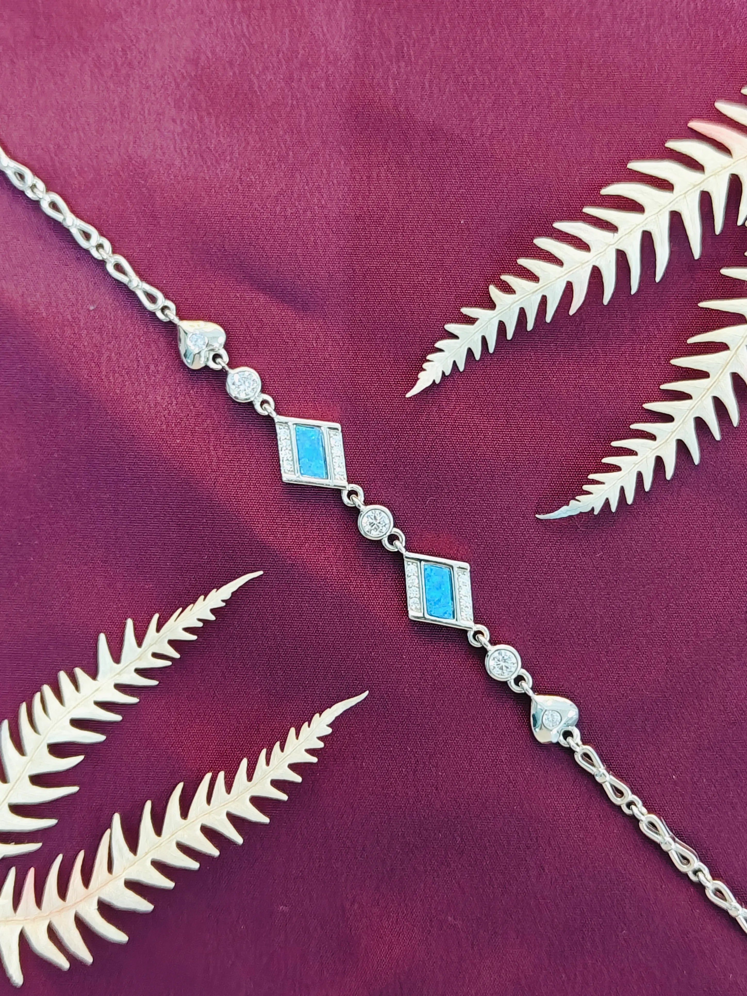 Silver chain necklace with blue accents on a purple fabric background with white leaves.